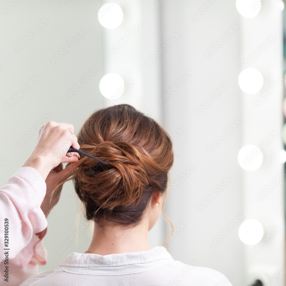 Fototapeta premium The work of the stylist on hairstyles in a bright salon, the girl makes curls and a bunch of beautiful model