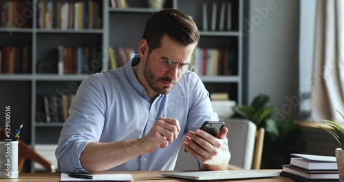 Mad unhappy businessman feeling annoyed using smart phone. Angry businessman having problem with mobile spam message. Male user frustrated by low battery or bad signal concept sitting at office desk.