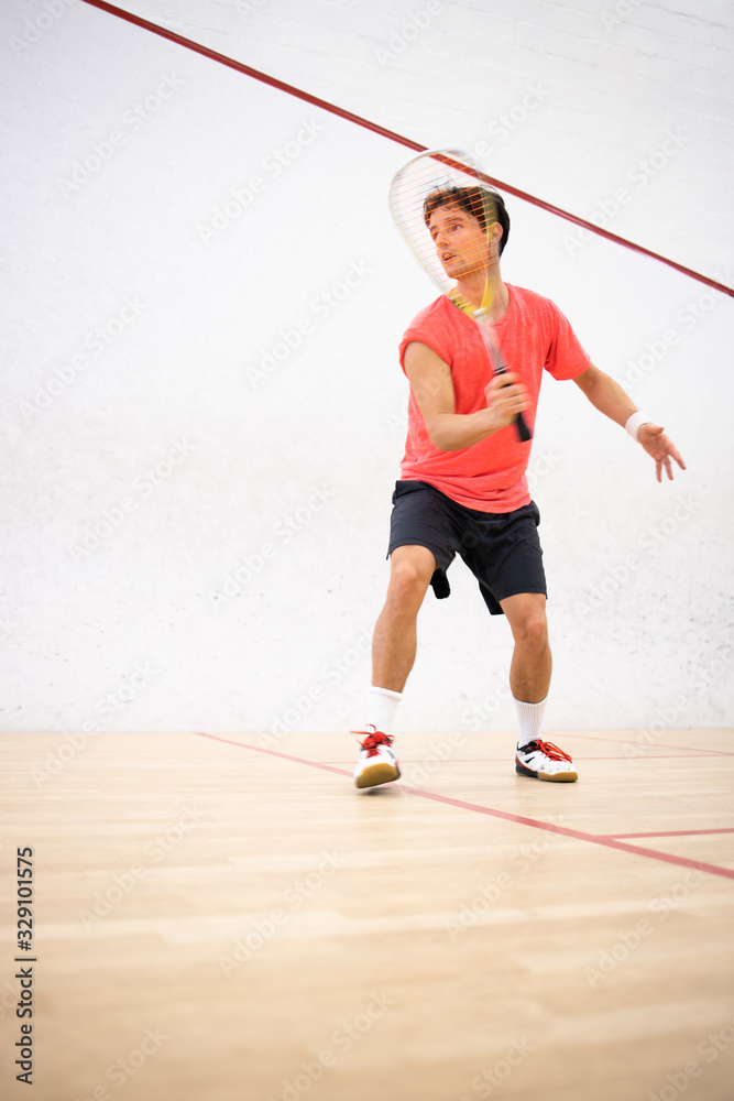 Squash player in action on a squash court (motion blurred image; color toned image)