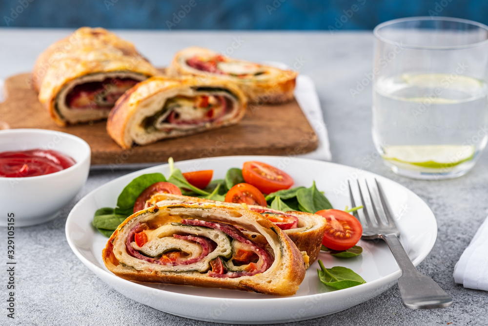 Italian food Pizza roll stromboli with cheese, salami, spinach and red pepper a light background. Italian food Pizza roll stromboli with cheese, salami, spinach and red pepper a light background.