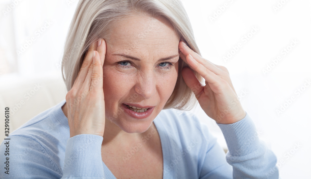 Woman suffering from stress or a headache grimacing in pain as she holds the back of her neck with her other hand to her temple, with copyspace. Concept photo with indicating location of pain.