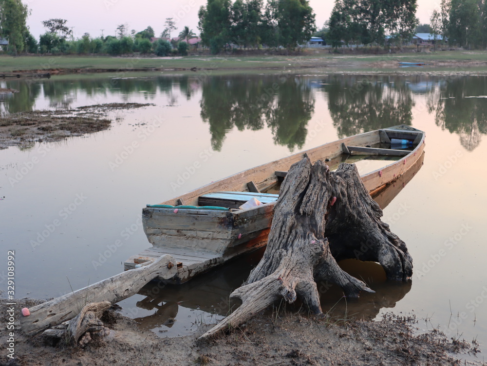 The old wooden boat moored along the river bank next to the stump.