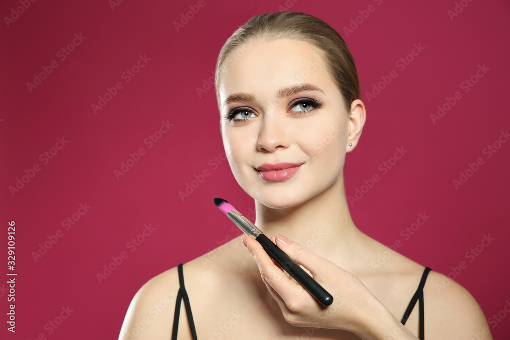 Artist applying makeup onto woman's face on pink background Artist applying makeup onto woman's face on pink background