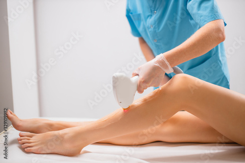 young slender, slim woman get epilation procedure in beauty salon. attractive lady sit in underwear while professional woman applying special ointment and use special machine for hair removal photo