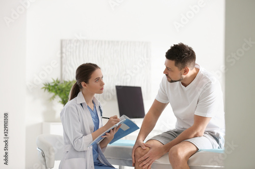 Female orthopedist examining patient with injured knee in clinic