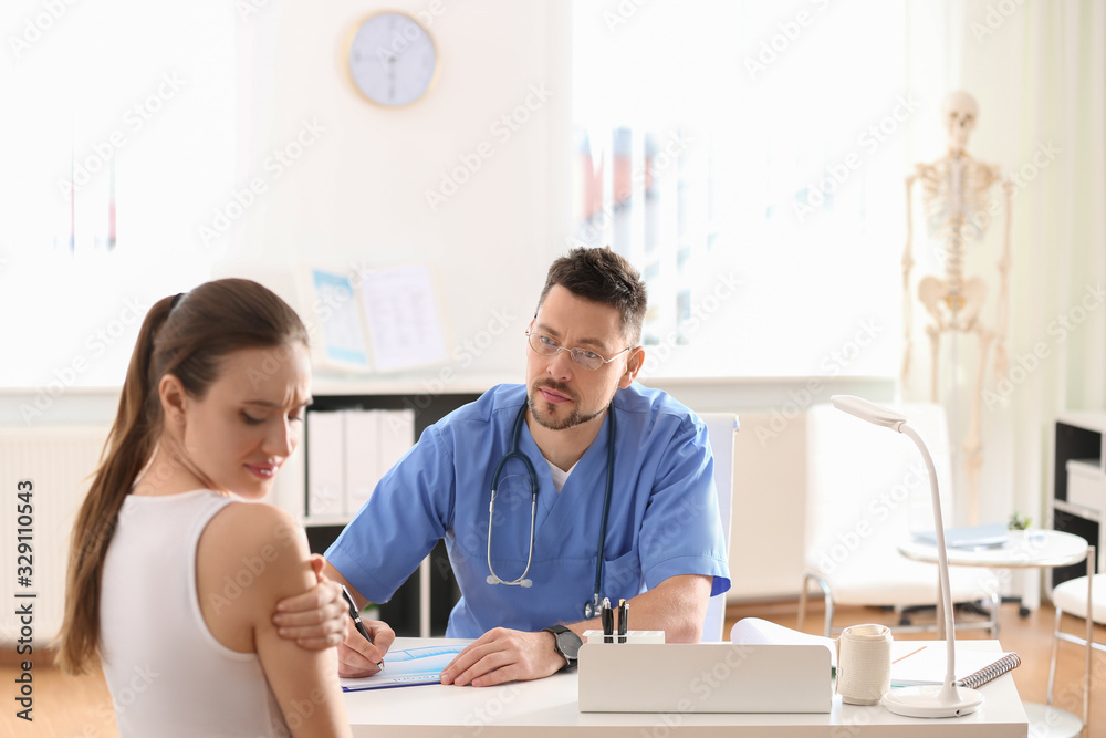 Male orthopedist examining patient with injured arm in clinic