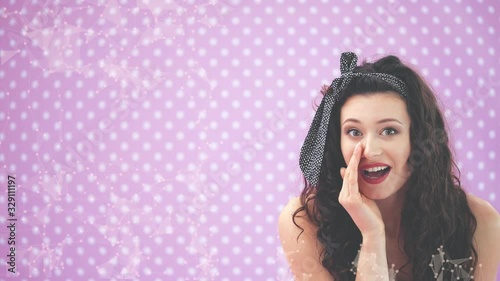 Adorable young girl in black polka-dots dress, leaning to the camera, whispering, pointing her finger to the side, showing tongue. photo