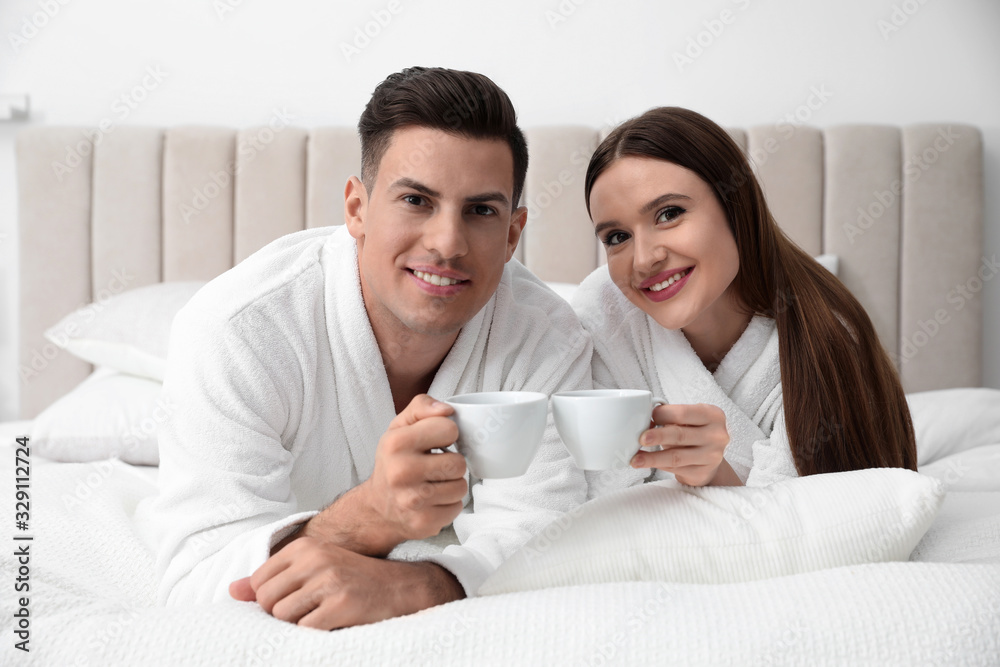 Happy couple in bathrobes with coffee on bed at home