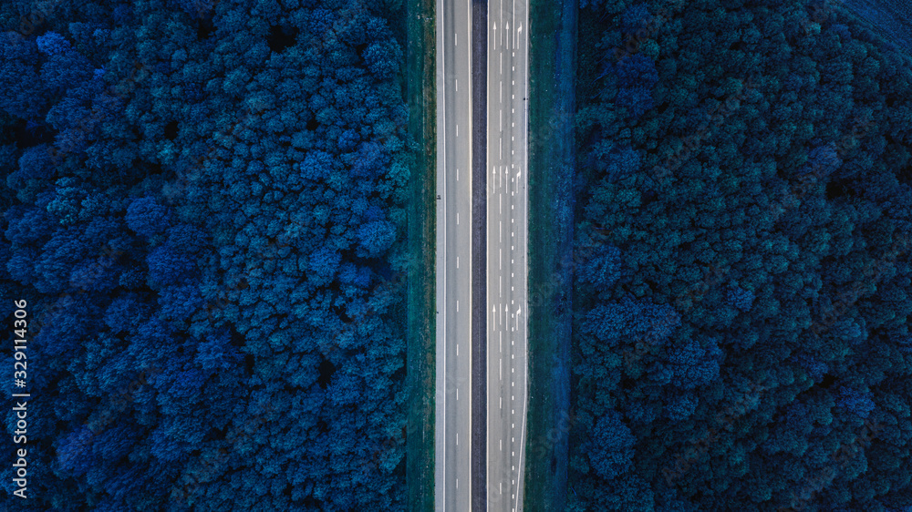 Aerial View Of Highway Road Through Blue Forest Landscaper.Toned Photo. Top View Flat View Of Highway Motorway Freeway From High Attitude. Trip And Travel Concept - obrazy, fototapety, plakaty 