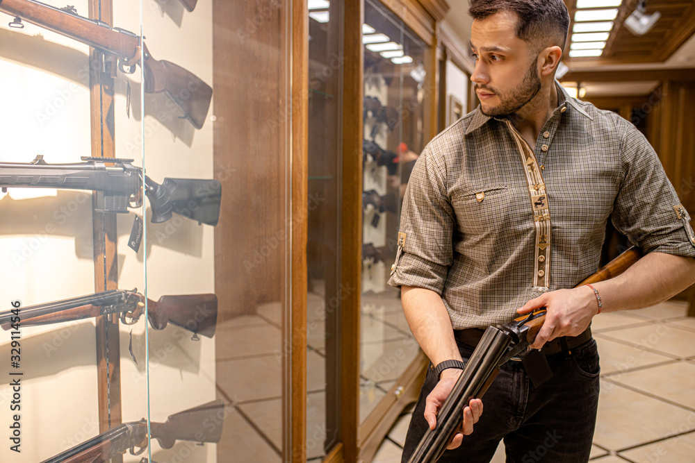 professional caucasian hunter looking for best rifle in guns store, he hold firearm in hands, want to make purchase professional caucasian hunter looking for best rifle in guns store, he hold firearm in hands, want to make purchase