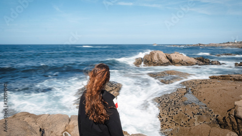 Girl with her back to the camera contemplating the sea with waves on a sunny day in Galicia, Spain