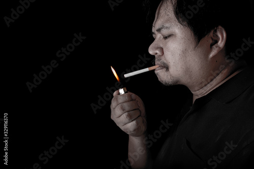The fat man lighting up a joint with lighter smoking at the black background, close up image of cigarette smoke spread in hand