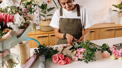 Smiling florist preparing a flower bouquet at her shop. Woman in apron working at counter. photo