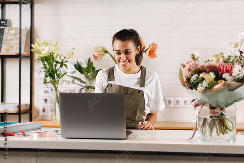 Photo Smiling flower shop owner working on laptop computer