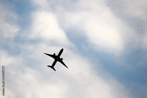 Airplane flying in the blue sky on background of white clouds. Silhouette of a commercial plane during the climb, travel and turbulence concept
