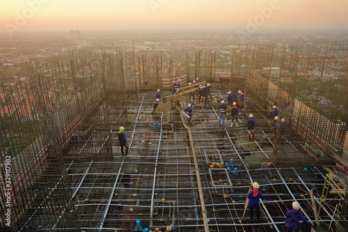 Many workers or labor are constructing high rise building as condominium, office, residence by pouring cement onto the steel has already been prepared on the rooftop beside the river, sunset, Bangkok