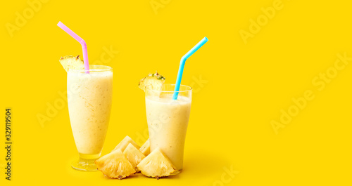 Fresh pineapple smoothie in two glasses and pineapple slices on a yellow background. Space for text