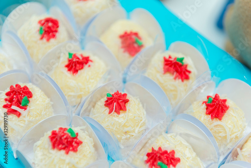 Coconut candy with icing grated coconut and red cream into paper box on blue tray.