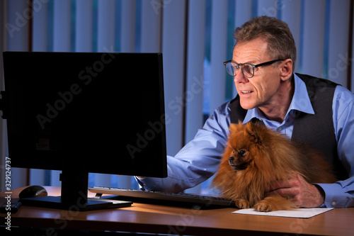 Mature businessman looking with his dog at computer sreen in an office at night photo