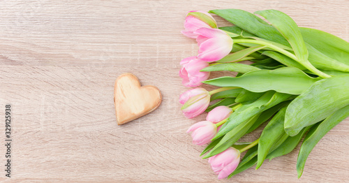 Rosarote Tulpen auf einem hellen Holztisch  mit Holzherz