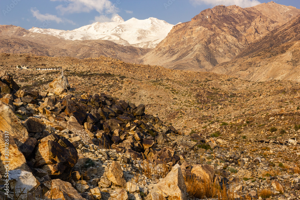Obraz premium A snow capped Himalayan peak towering over the rocky slopes of the dry, barren mountains in the village of Nako in Kinnaur in Himachal Pradesh, India.