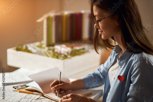 concentrated businesswoman working on blueprint in office, close up side view photo. girl writing her ideas, planning her working day in the office. layout in the blurred background of the photo