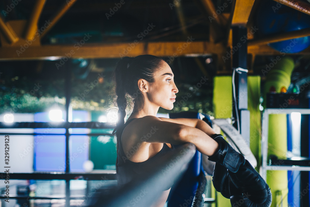 Fototapeta premium Female kickboxer resting on ring corner. 