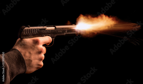 The hand presses the trigger of the gun and the flame from the shot escapes from its muzzle