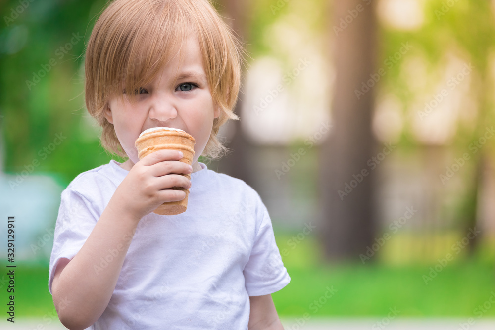 Beautiful baby with blue eyes in white tshirt is eating glass of white ice cream.