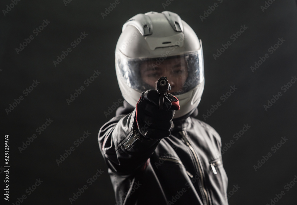 A bandit in a motorcycle helmet and leather jacket with a gun