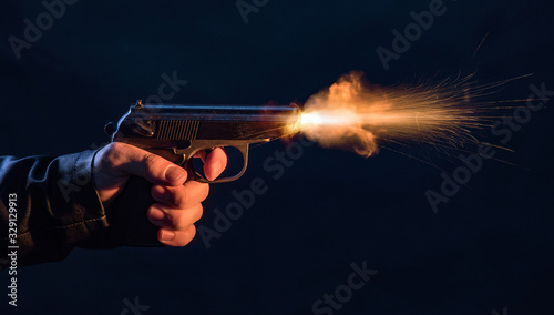 Obraz na plátně The hand presses the trigger of the gun and the flame from the shot escapes from