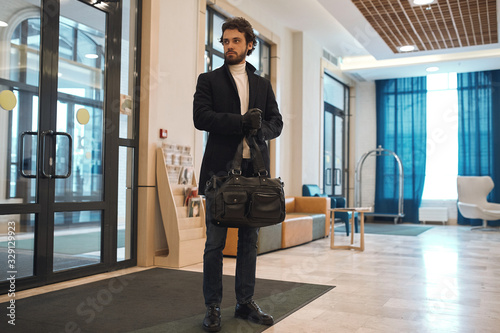 elegant man with a hand bag wearing a black stylish coat waiting for a client. man selling goods, drugs, full length photo, business