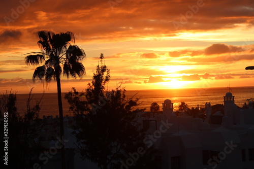 Sunny sunset on the background of the Atlantic Ocean, clouds, white Tenerife hotels and palm trees