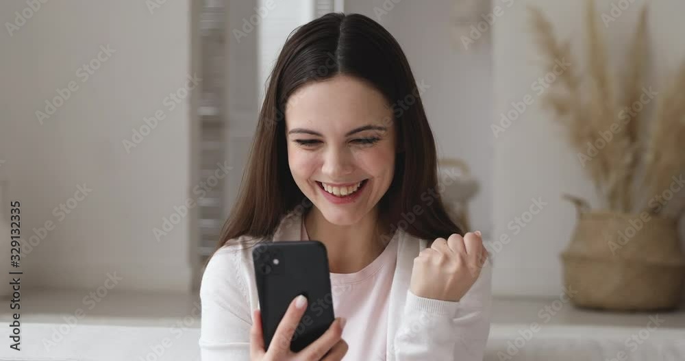Excited young woman holding smart phone reading good news in social media feed receiving sms message. Overjoyed happy girl user winning auction bid or mobile app game celebrating success concept Excited young woman holding smart phone reading good news in social media feed receiving sms message. Overjoyed happy girl user winning auction bid or mobile app game celebrating success concept