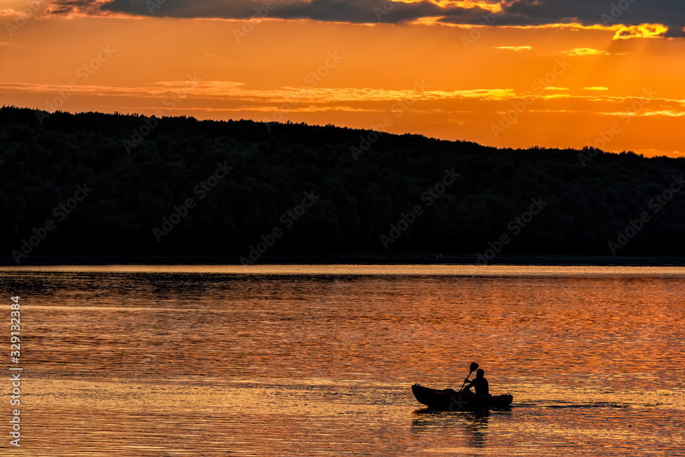 Silhouette of a sailor in a kayak canoe on the lake in the sunset light near an island, Danube River, Dobrogea, Romania