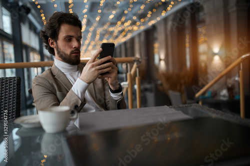 serious elegant guy using his smart phone while having a rest at the cafe. close up photo. free time, spare time, lifestyle , blurred foreground, technology, gadget