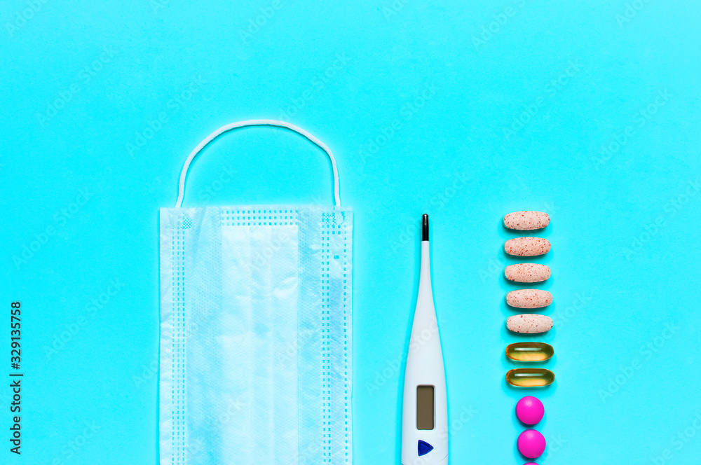 Medical mask, electronic thermometer, pills or vitamins on blue background flat lay top view copy space. Protection against virus, coronavirus, flu, colds, diseases. Concept of health. Allergy season