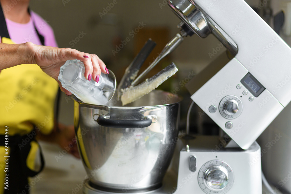 Woman professional pastry chef preparing a dessert. Adds ingredients and mixes the dough in a mixer
