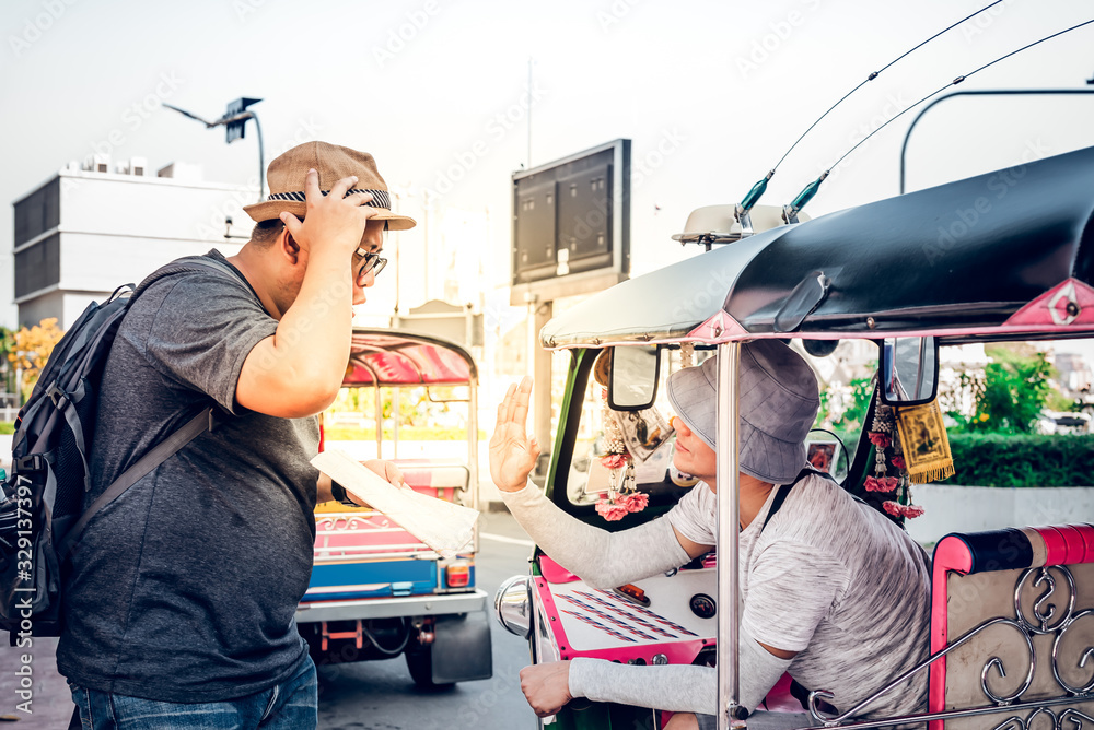 Asian tourists Is negotiating a fare with a tuk tuk driver, along the travel route on the map he holds in his hand, concept to summer and travel on vacation at Thailand Asian tourists Is negotiating a fare with a tuk tuk driver, along the travel route on the map he holds in his hand, concept to summer and travel on vacation at Thailand