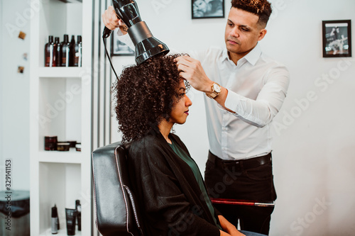 Beautiful latin woman with short curly brown hair getting a treat at the hairdresser. Latin hairdresser working her afro hair. Lifestyle