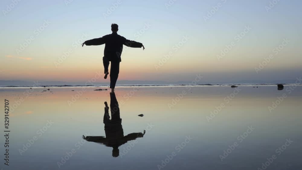 Silhouette of man practicing the elements of qigong at sunset by the sea Silhouette of man practicing the elements of qigong at sunset by the sea