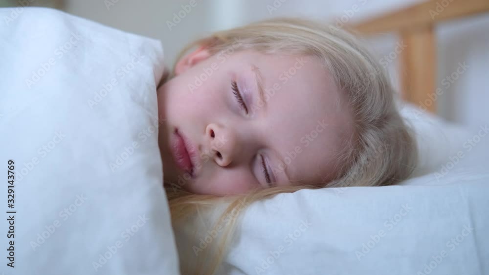 Sleeping little blonde girl close up in big bed with white bedding early in the morning. Children dream. Childhood, calm, night .4k footage Sleeping little blonde girl close up in big bed with white bedding early in the morning. Children dream. Childhood, calm, night .4k footage