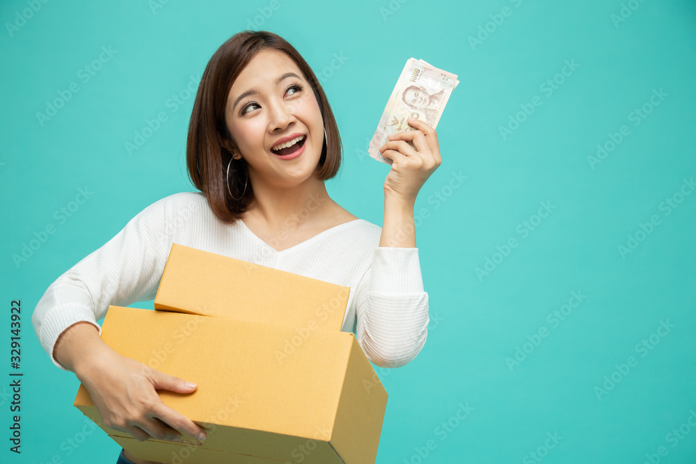Happy Asian woman holding package parcel box and celebrating with money banknotes thai baht isolated on green background, Delivery courier and shipping service concept Happy Asian woman holding package parcel box and celebrating with money banknotes thai baht isolated on green background, Delivery courier and shipping service concept