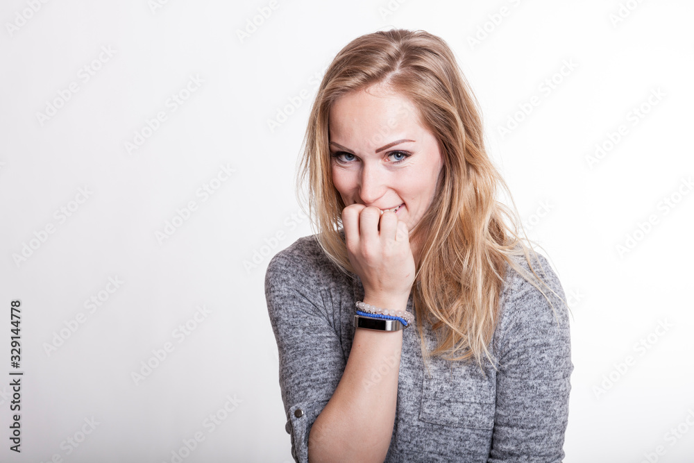 Nervöse blonde Frau guckt verlegen und kaut an ihren Fingernägeln Nervöse blonde Frau guckt verlegen und kaut an ihren Fingernägeln