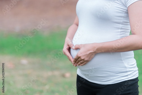 Portrait of asian Beautiful pregnant woman at the park,Thailand people,Happy woman concept,Her use hand touch her belly,She make hand shape heart