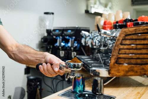 Detail of man hand holding portafilter recipient filled with coffee ground while preparing espresso