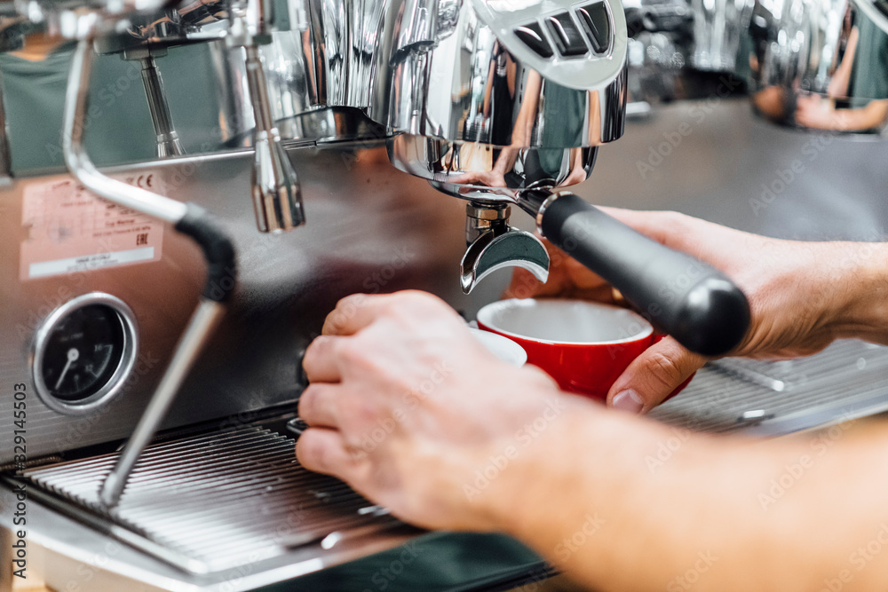 Close-up shot of barista holding filter holder while coffee machine brewing fresh espresso into glass