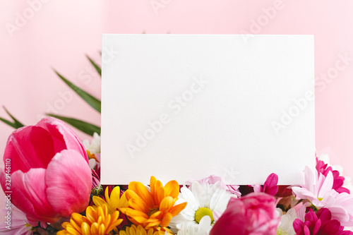 Flowers mock up congratulation. Congratulations card in bouquet of flowers on pink background. White blank card with space for text, frame mockup. Spring festive flower concept, gift card.