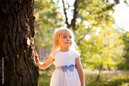 Cute little girl leaning against big tree in summer