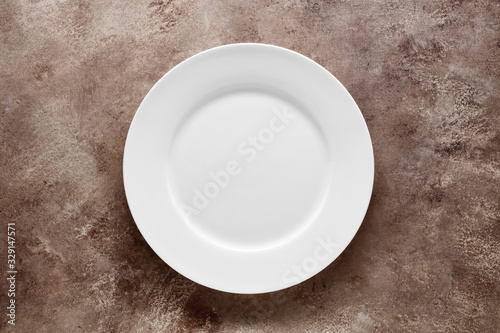 Empty white plate on brown textured background with copy space